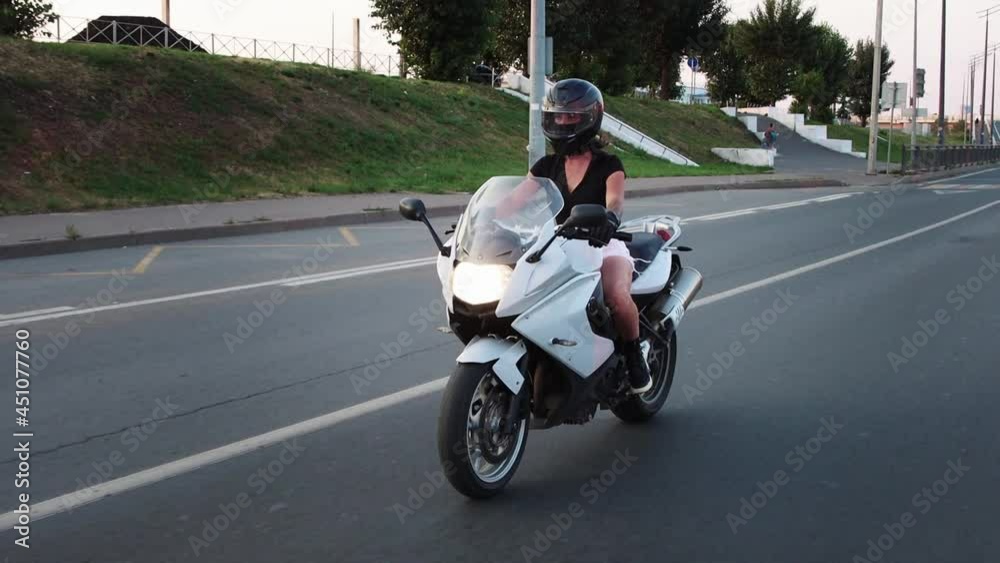 A woman is riding motorcycle at early sunset - raises the glass of the protective helmet A woman is riding motorcycle at early sunset - raises the glass of the protective helmet