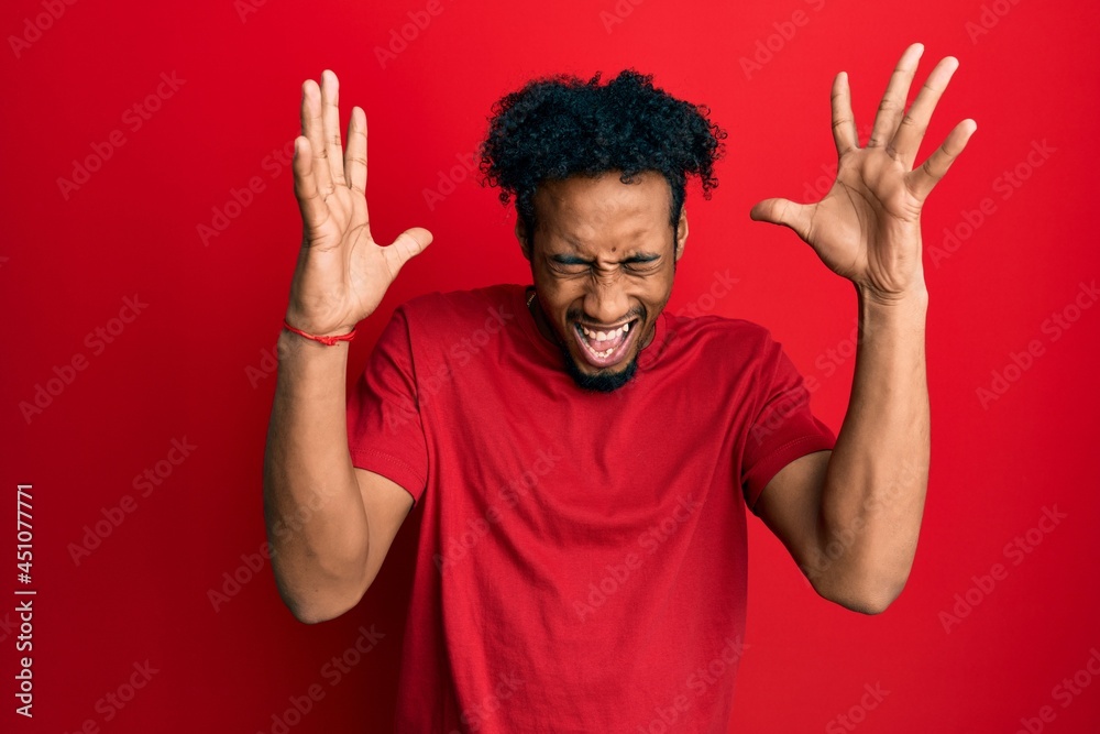 Young african american man with beard wearing casual red t shirt celebrating mad and crazy for success with arms raised and closed eyes screaming excited. winner concept Young african american man with beard wearing casual red t shirt celebrating mad and crazy for success with arms raised and closed eyes screaming excited. winner concept