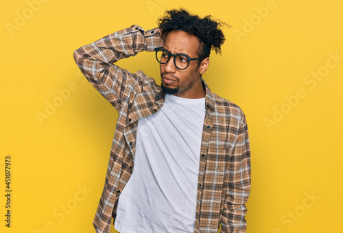 Young african american man with beard wearing casual clothes and glasses confuse and wondering about question. uncertain with doubt, thinking with hand on head. pensive concept.