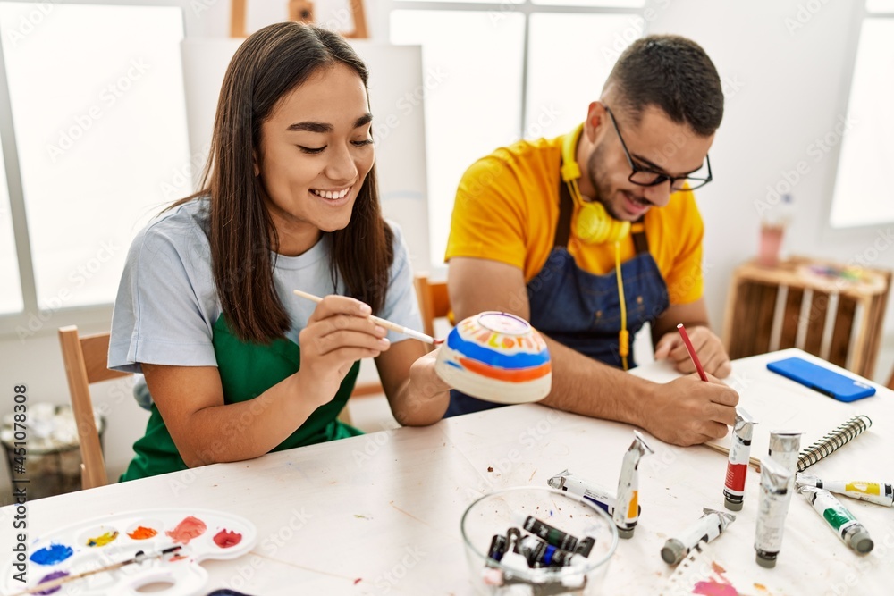 Young hispanic couple smiling happy drawing sitting on the table at art studio. Young hispanic couple smiling happy drawing sitting on the table at art studio.