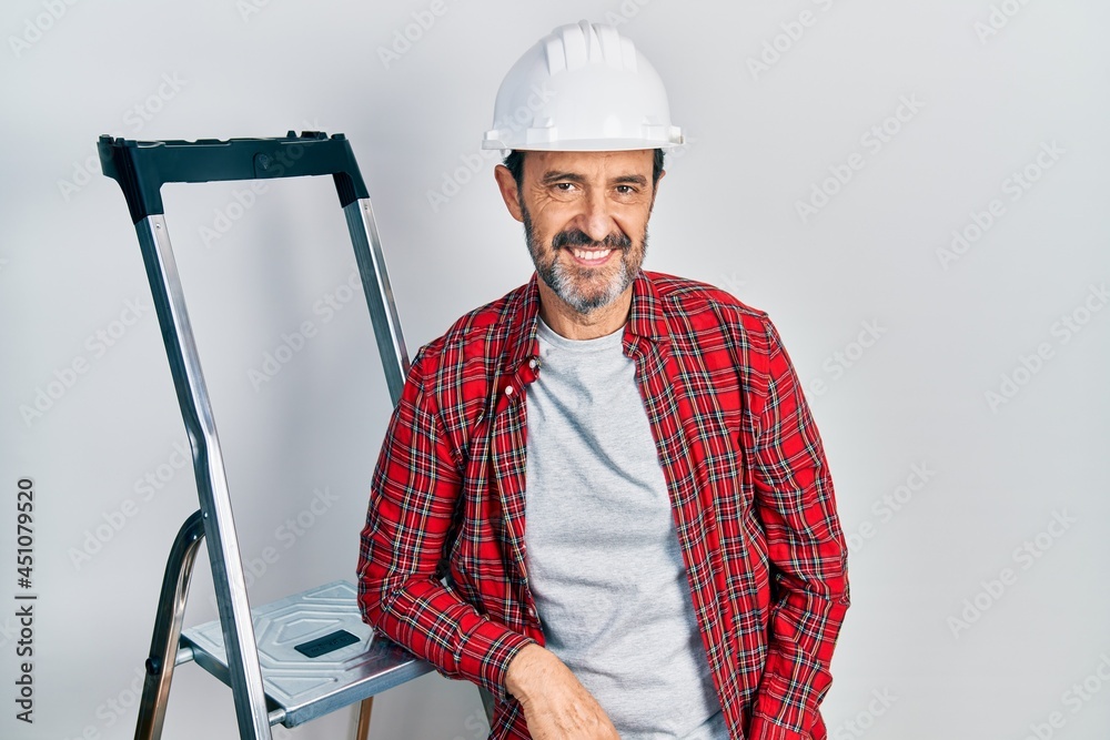 Middle age hispanic worker man using ladder looking positive and happy standing and smiling with a confident smile showing teeth Middle age hispanic worker man using ladder looking positive and happy standing and smiling with a confident smile showing teeth