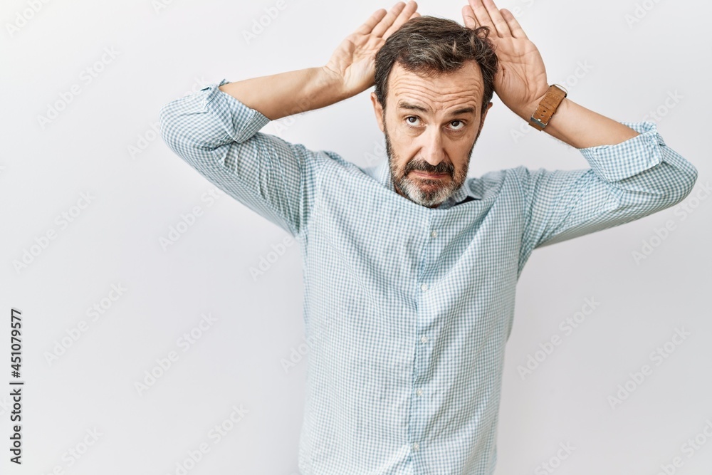 Middle age hispanic man with beard standing over isolated background doing bunny ears gesture with hands palms looking cynical and skeptical. easter rabbit concept. Middle age hispanic man with beard standing over isolated background doing bunny ears gesture with hands palms looking cynical and skeptical. easter rabbit concept.