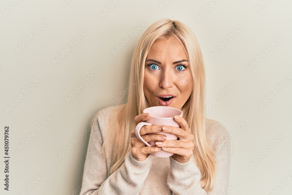 Young blonde woman drinking a cup of coffee afraid and shocked with surprise and amazed expression, fear and excited face. Young blonde woman drinking a cup of coffee afraid and shocked with surprise and amazed expression, fear and excited face.