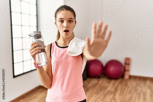 Young brunette teenager wearing sportswear holding water bottle doing stop gesture with hands palms, angry and frustration expression