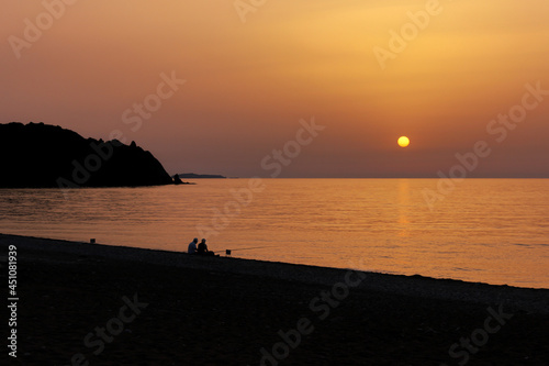 Silhouette of two men fishing on the beach during the sunrise. Sun rises over the Mediterranean Sea on a lovely summer morning. Selective focus.