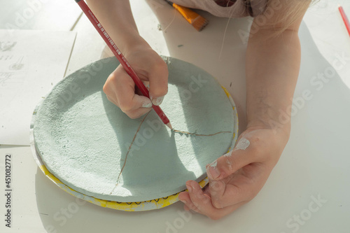 kid hand painting with pencil on colored clay pottery cup in ceramic workshop studio. Development of art and painting in children. Close-up