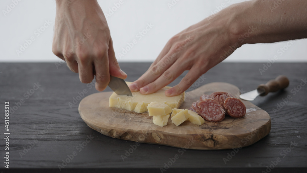 Man cuts some vintage cheese next to cured sausage on olive board with copy space
