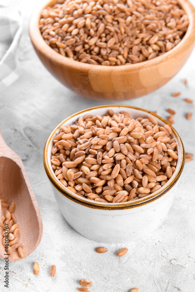 Wholegrain uncooked raw spelt farro in the bowls on grey stone table background, food cereal background, close up Wholegrain uncooked raw spelt farro in the bowls on grey stone table background, food cereal background, close up