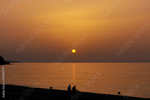 Silhouette of two men fishing by the seaside at dawn. Sun rises over the Mediterranean Sea in Cirali, Antalya, Turkey. Selective focus.