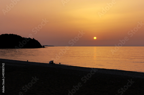 Silhouette of two men fishing by the seaside at dawn. Sun rises over the Mediterranean Sea in Cirali, Antalya, Turkey. Selective focus.