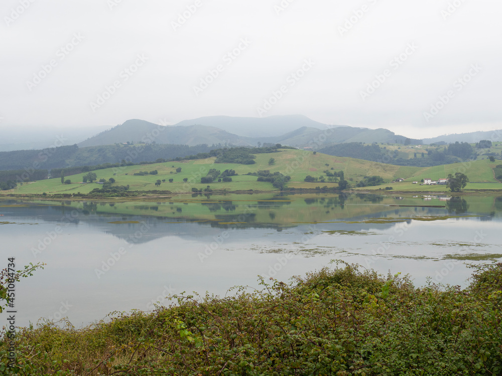 Paisaje marítimo de brumas sobre las montañas reflejadas en el agua en el Camping El Rosal de Cantabria, España en verano de 2020.
