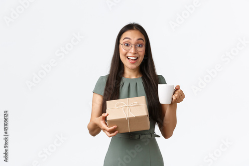 Excited happy asian woman drinking coffee and receive home delivery, holding box package with cheerful smile, finally receiving order from online shop, standing white background photo