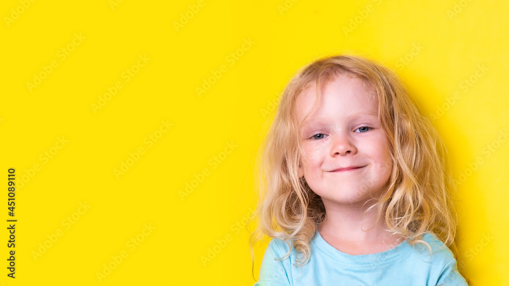 portrait beautiful curly funny little girl with blond curly hair wearing blue t-shirt on yellow background with copy space portrait beautiful curly funny little girl with blond curly hair wearing blue t-shirt on yellow background with copy space
