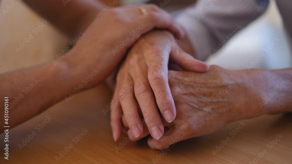 Worried caucasian man gently stroking hand of his sick old mother showing care or love. Son comforting wrinkled arm of elderly mom sitting at bed. Guy giving support to his old parent slow motion.