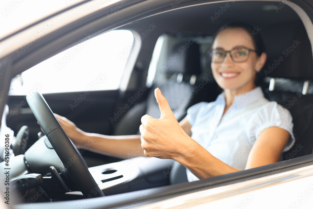Woman sitting behind wheel of car and showing thumb up closeup