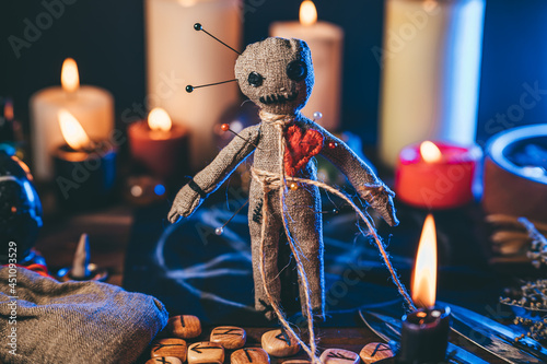 Voodoo doll studded with needles in magical table with candles and occult objects. Magic and dark spooky ritual. Retribution or revenge through witchcraft concept. photo