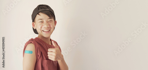 Mixed Asian teen boy giving thumb up and showing his arm with blue bandage after got vaccinated or  inoculation, child immunization, covid delta vaccine concept photo