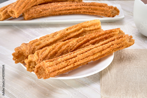 spanish churros covered with sugar and cinnamon on a white plate on a marble surface and white background. close up view.