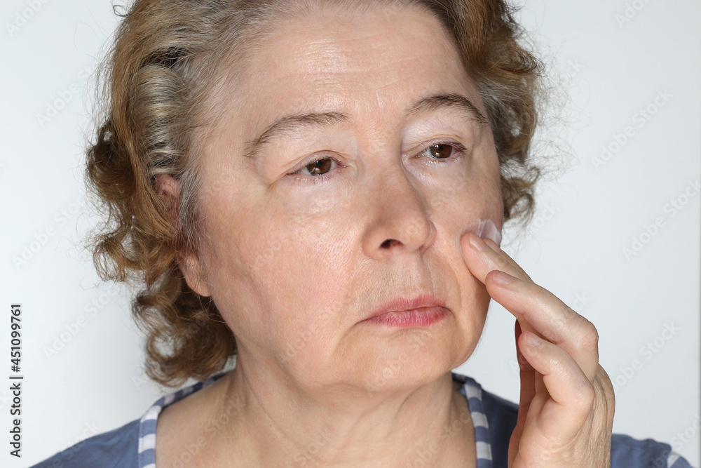 Elderly woman cares for her face applies anti-aging cream to her face Elderly woman cares for her face applies anti-aging cream to her face