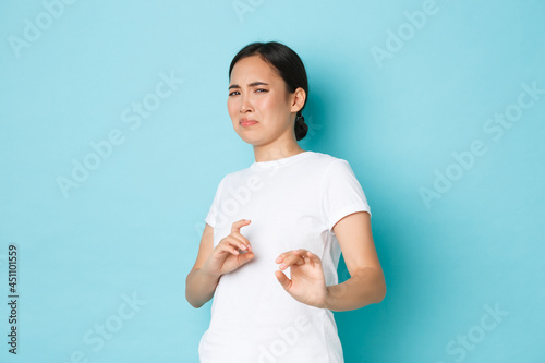 Disgusted and displeased asian girl exressing aversion and reluctance, grimacing and raising hands defensive, stay away, refusing offer, rejecting something, standing blue background photo