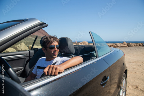 Indian rich man sitting in his convertible car wears sunglasses and looks to the side. Realized man sitting in an expensive car. Forty year old person of indian ethnicity