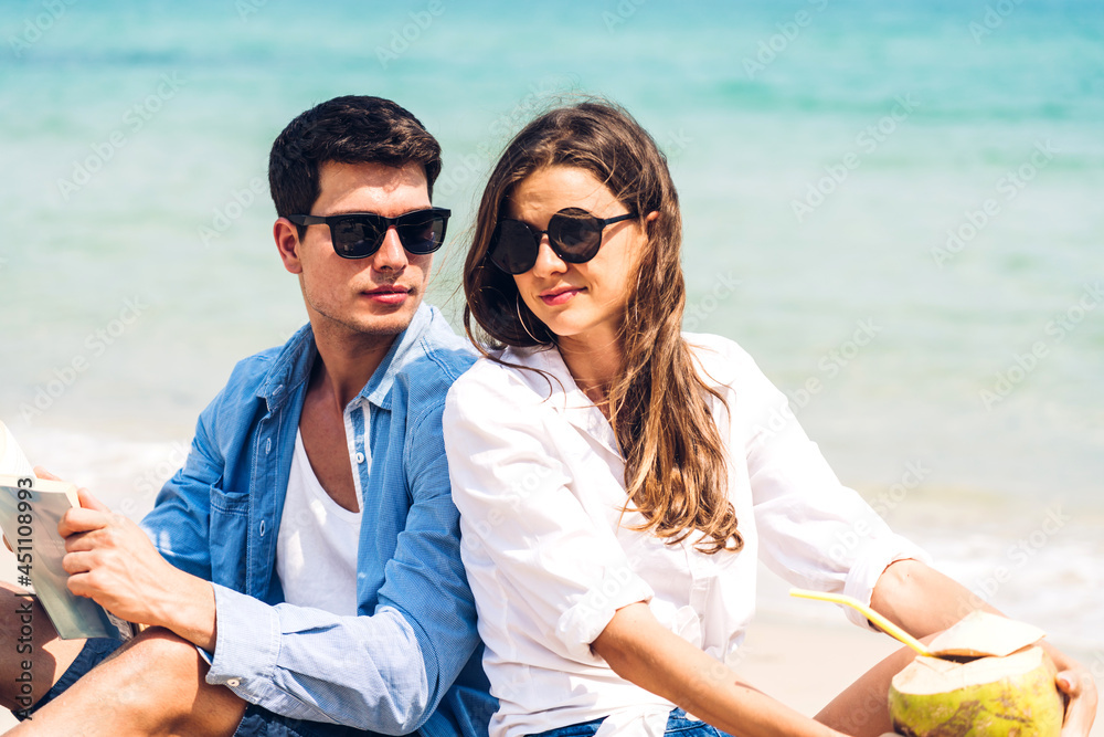 Young couple drinking coconut juice and reading a book on the tropical beach.Couple relaxing on the beach.Summer vacations Young couple drinking coconut juice and reading a book on the tropical beach.Couple relaxing on the beach.Summer vacations