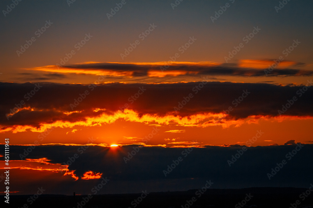 Fototapeta premium the bright sun peeks out from behind the clouds at dawn on a warm summer morning