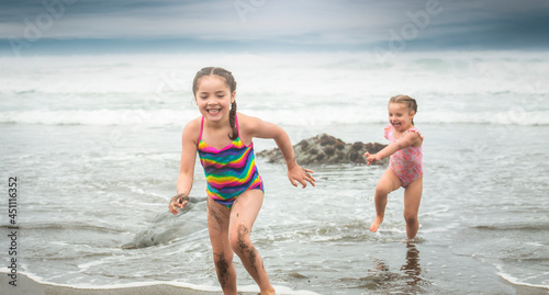 Big sister running from ocean waves with laughing little sister behind
