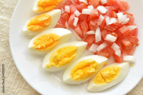 Boiled egg salad with tomatoes and onions on a white plate. The concept of healthy and dietary food. Flat lay top view photo. Food from above. 