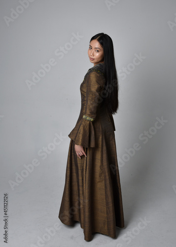 Full length portrait of beautiful young asian woman with long hair wearing medieval fantasy gown costume. Graceful standing posing walking away, isolated on studio background.