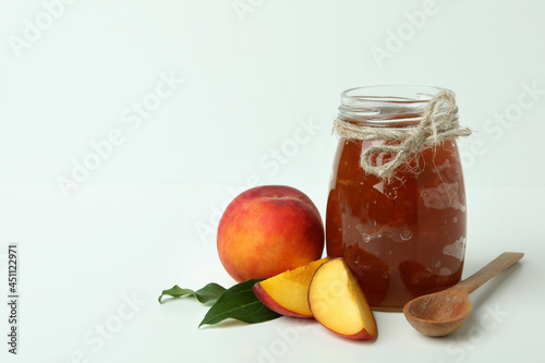 Jar of peach jam, ingredients and spoon on white table