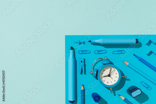 Top view photo of ordered school supplies blue stationery felt pens pencils clips pushpins and alarm clock on isolated light blue background with empty space