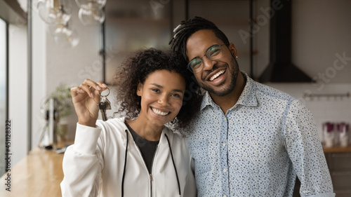 Happy homeowners smiling African married young couple standing in modern kitchen holding keys posing on camera. Moving day, own apartment, housing improvement, bank loan, affordable dwelling concept photo