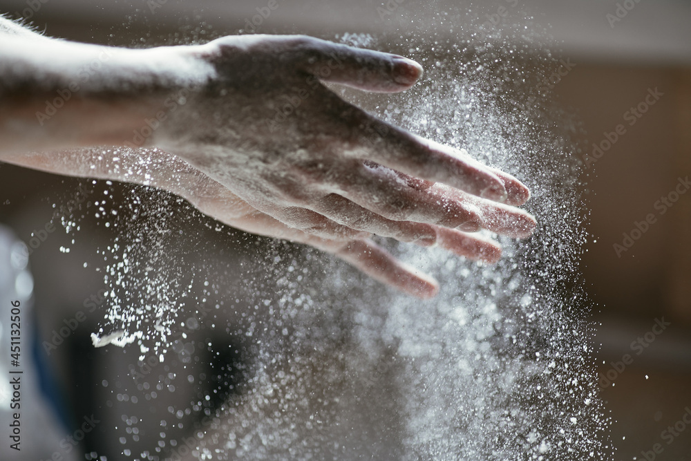 Fototapeta premium Glowing particles of flour in the air and a woman's hand close-up, photo of a hand in motion, blurred background