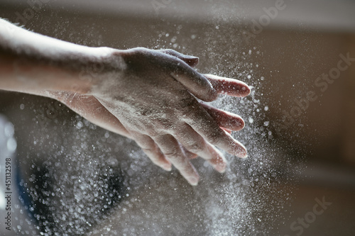 Girl shakes flour off her hands, flour particles illuminated by the backlight from the window