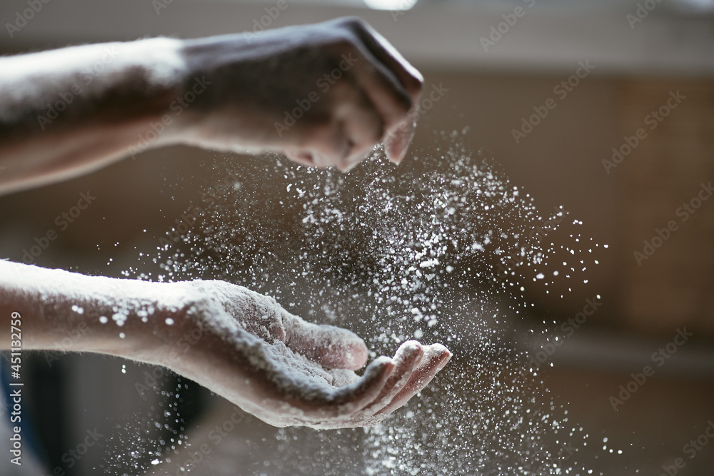 Fototapeta premium Girl scattering flour in the air, close-up photo of hands