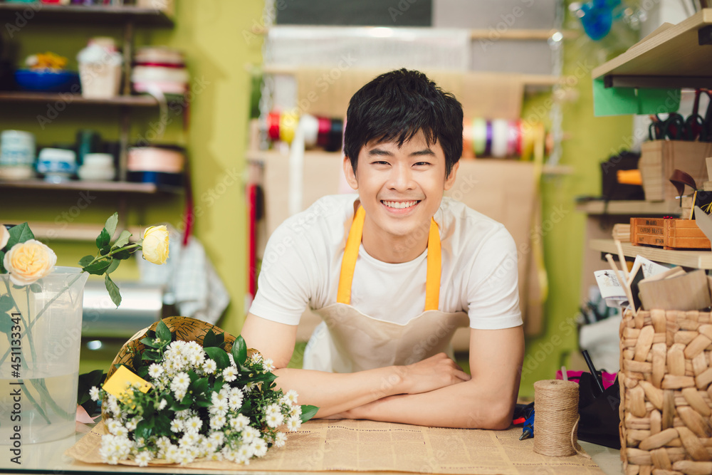 Fototapeta premium Male florist in flower shop. Man in apron is cutting stems and preparing roses for a bouquet. Owner of the flower shop, doing small business.