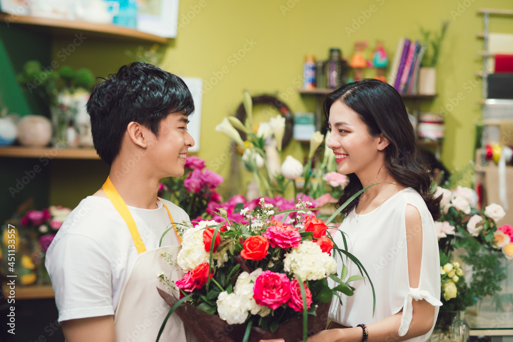 Asian woman buying a bouquet of fresh flowers and smiling at the store assistant in a flower shop