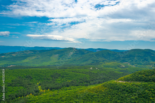 Crimean mountains covered with green forest against a blue sky with white clouds