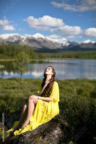 beautiful girl, brunette in a yellow dress walks near a mountain lake