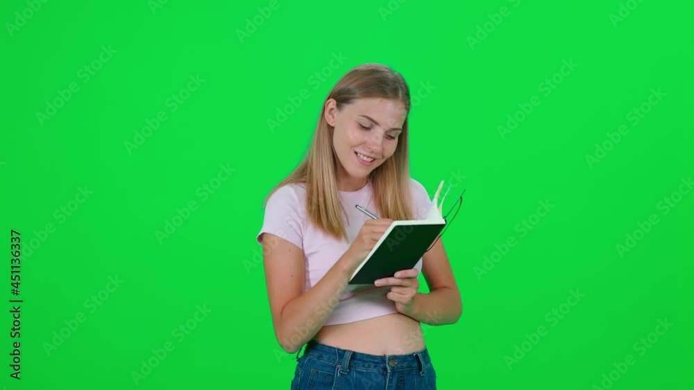 Caucasian female writes down successful ideas in a notebook, an emotional blonde woman standing on a green background, a chroma key template. Caucasian female writes down successful ideas in a notebook, an emotional blonde woman standing on a green background, a chroma key template.