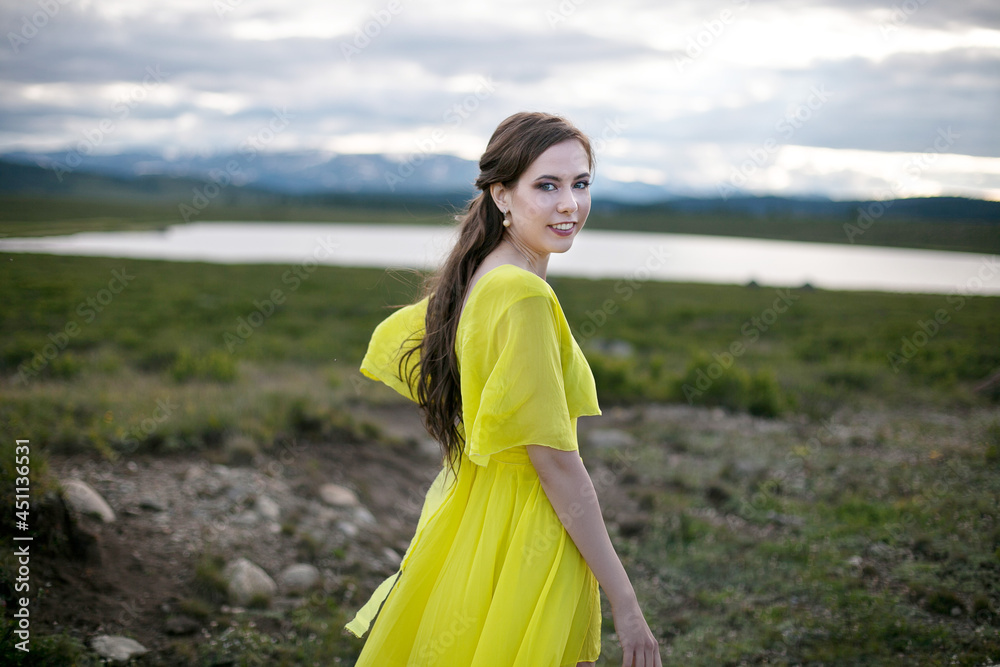 beautiful girl, brunette in a yellow dress walks near a mountain lake beautiful girl, brunette in a yellow dress walks near a mountain lake