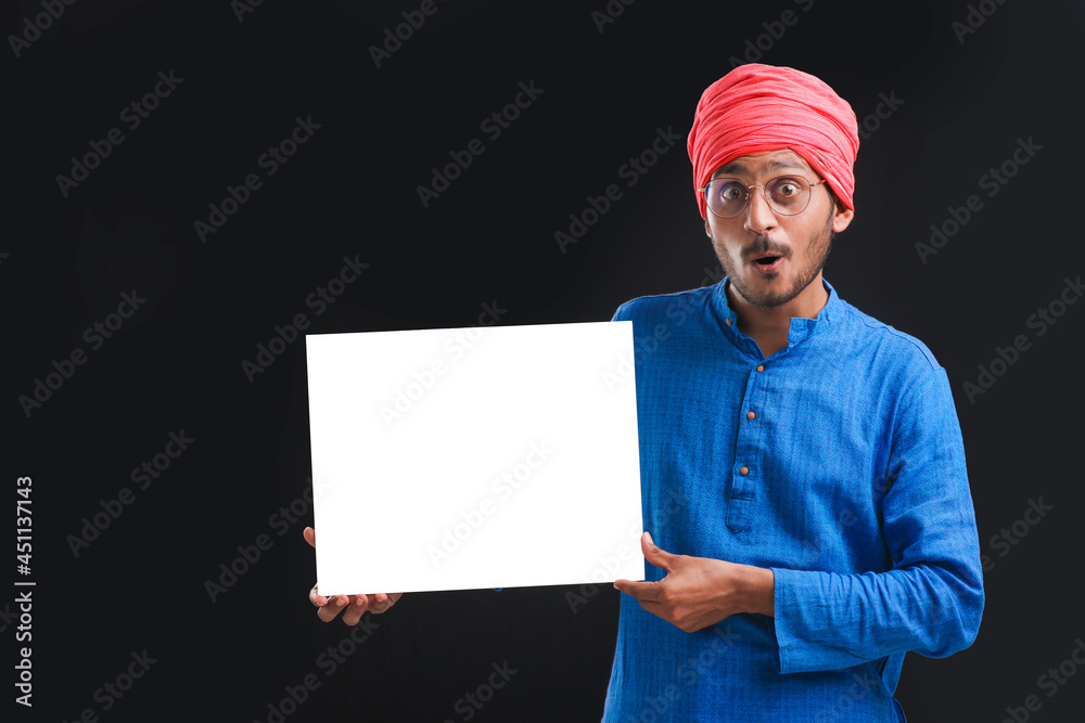 Young indian farmer holding white card board on dark background. Young indian farmer holding white card board on dark background.