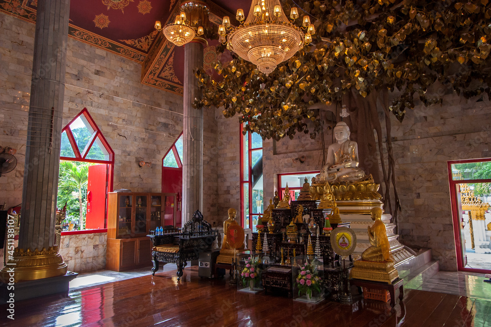Altar with Buddha statue and other decorations in Buddhist temple. Wish tree and large luminous chandeliers.