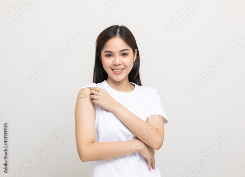 Vaccination. Young beautiful asian woman getting a vaccine protection the coronavirus. Smiling happy female showing arm with bandage after receiving vaccination. On isolated white background. © Chanakon