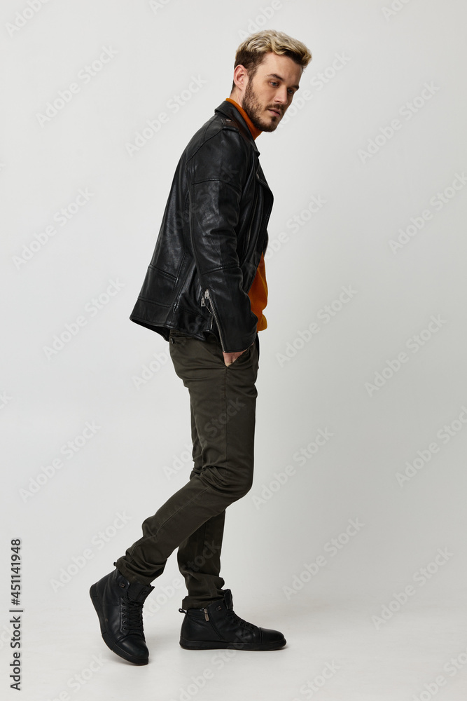 a man in a leather jacket, orange sweater and trousers turned to the side on a Light background copy Copy Space a man in a leather jacket, orange sweater and trousers turned to the side on a Light background copy Copy Space