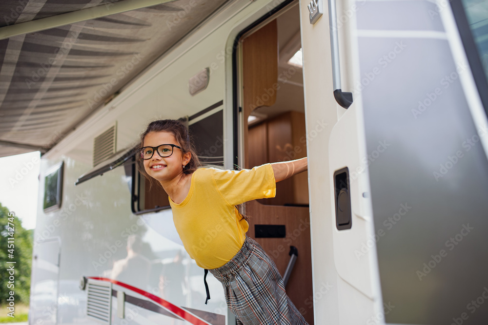 Happy small girl standing by caravan door, family holiday trip. - obrazy, fototapety, plakaty 