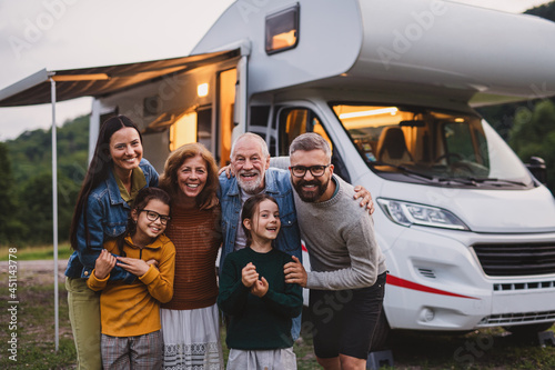 Multi-generation family looking at camera outdoors at dusk, caravan holiday trip Fototapete