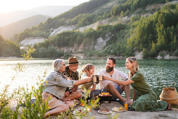 Happy multigeneration family on summer holiday trip, barbecue by lake.