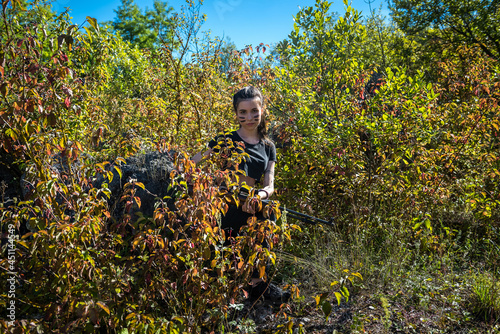 pretty female hunter in top in forest with weapon in nature.